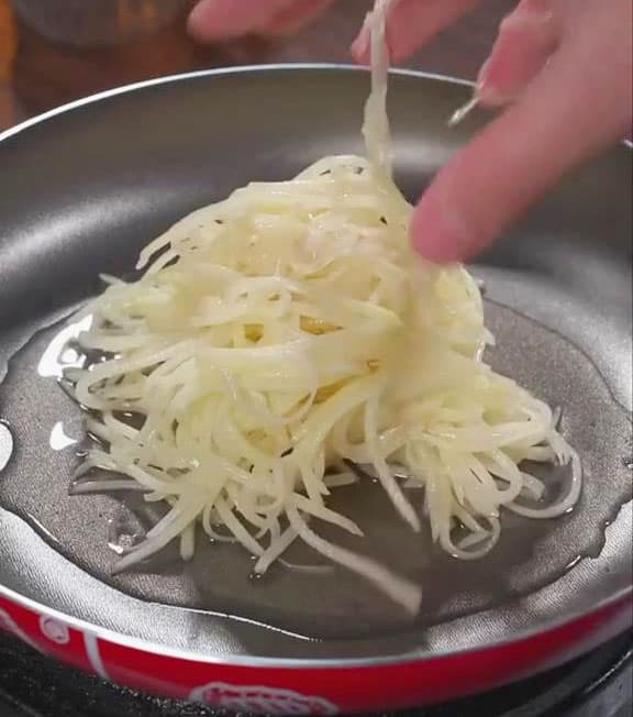 Take a handful of the seasoned shredded potatoes and place it into the pan